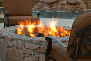 Outdoor stone fire pit with flames and patio chairs